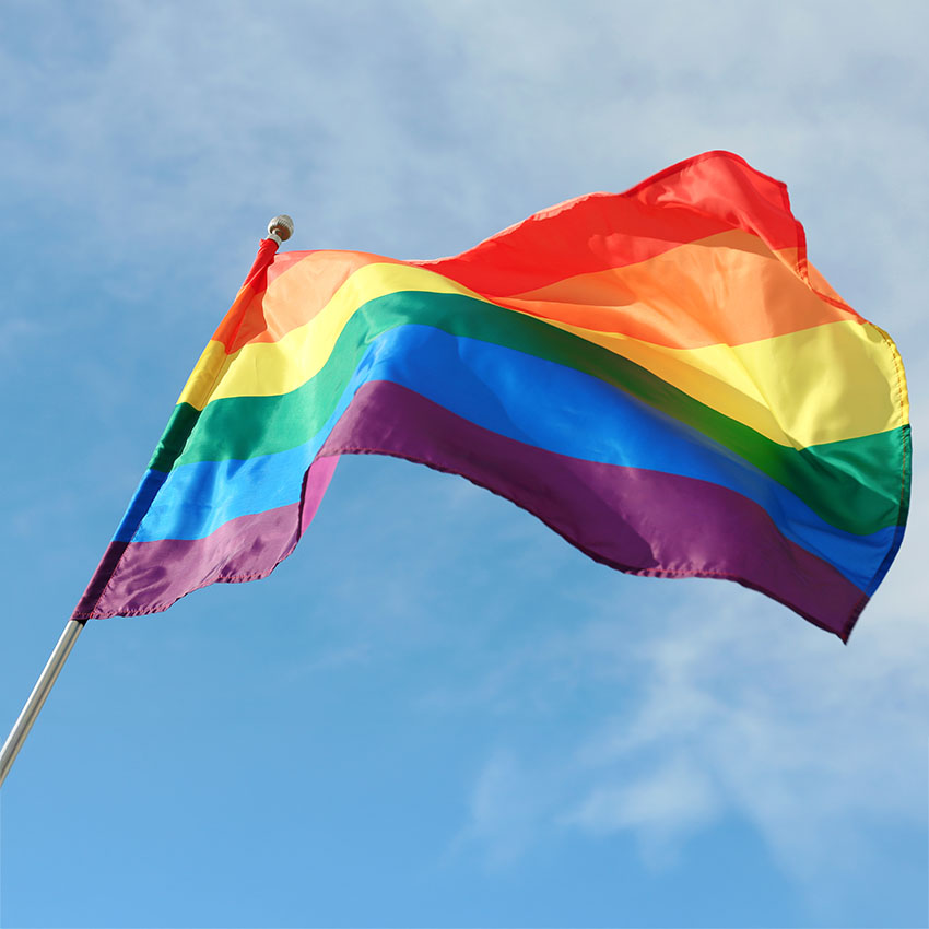 LGBT rainbow flag flying in wind against a blue sky to show counselor as a LGBTQ+ Ally