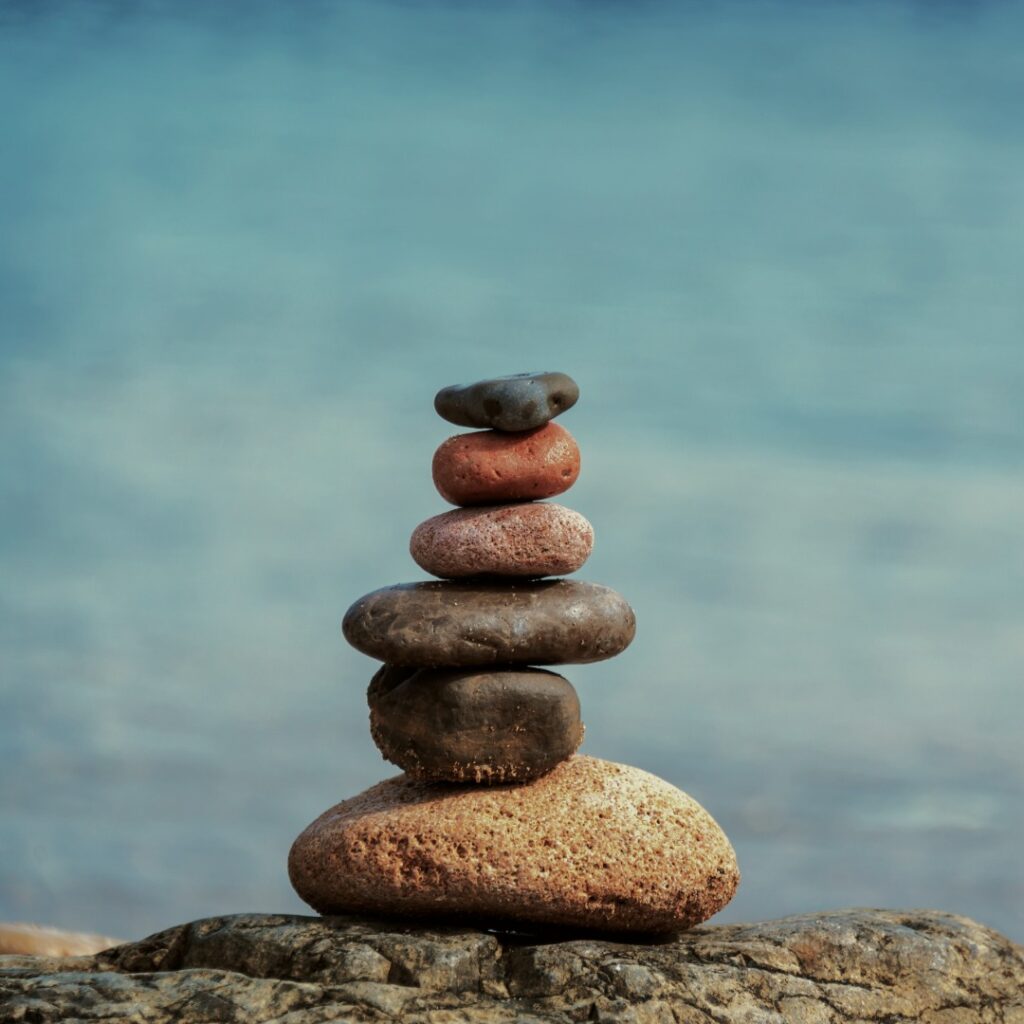 Smooth, spa rocks stacked a lake in background to show internal calm and peace resulting from seeing a counselor or therapist for stress management.
