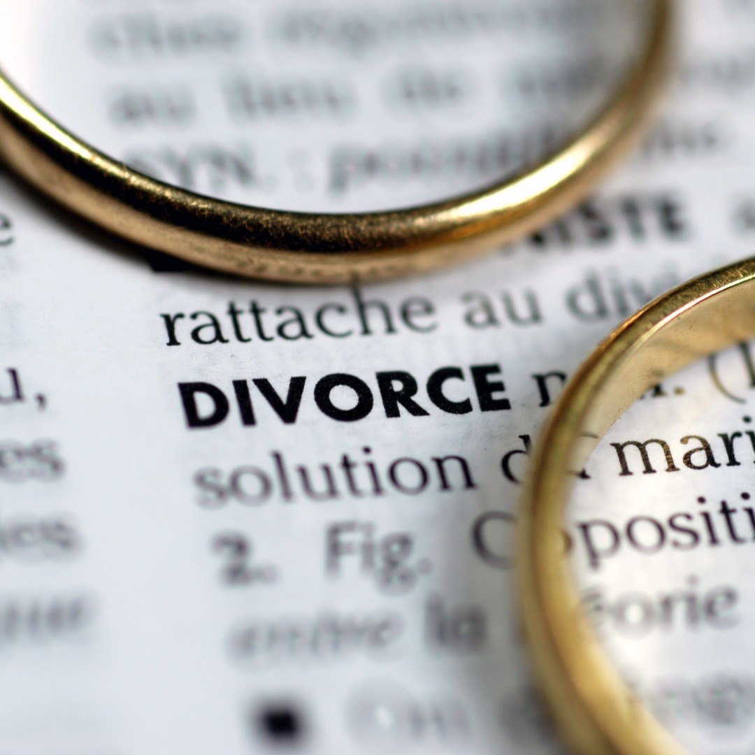 Two wedding rings laying on top of a dictionary page for Divorce to represents the loss and mourning a grief that a counselor and therapy can help with.