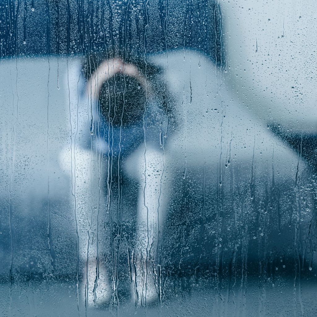 raining view looking in window on depressed woman sitting on bed